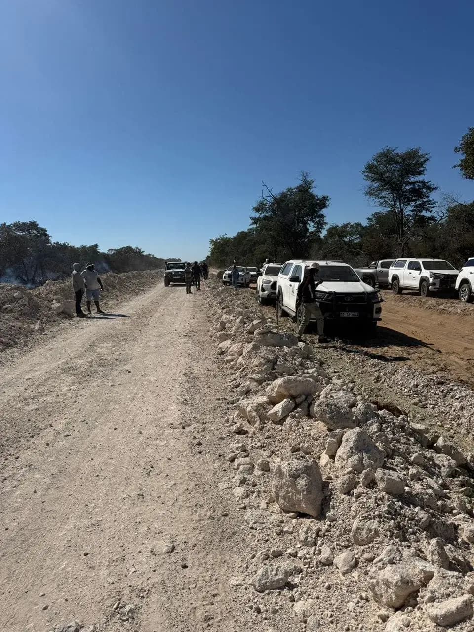 Vehicles and people gathered beside an unpaved work route