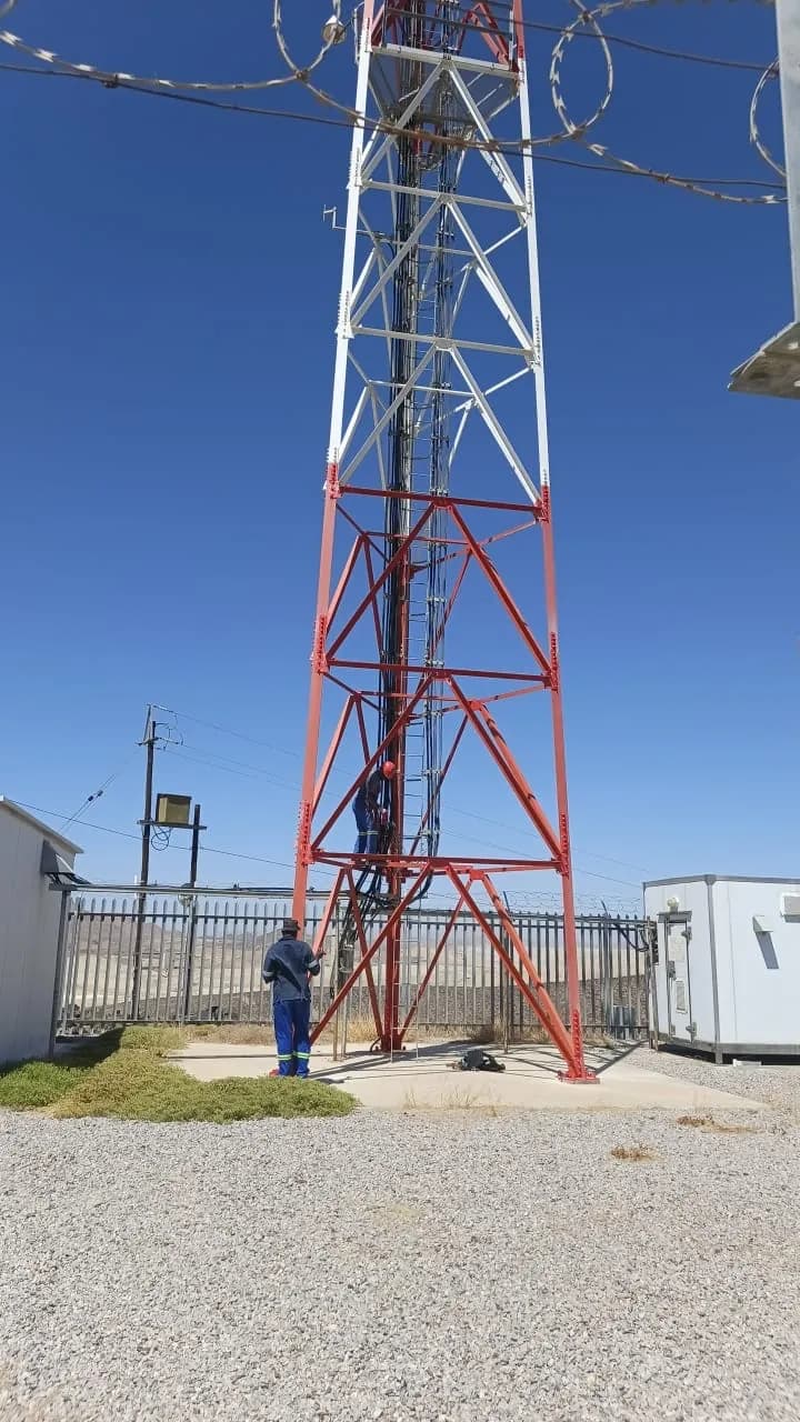 Red and white communications mast above a prepared site